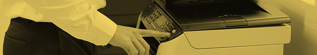 A person in a dress shirt is pressing buttons on a refurbished printer in an office setting. The image has a yellowish tint.