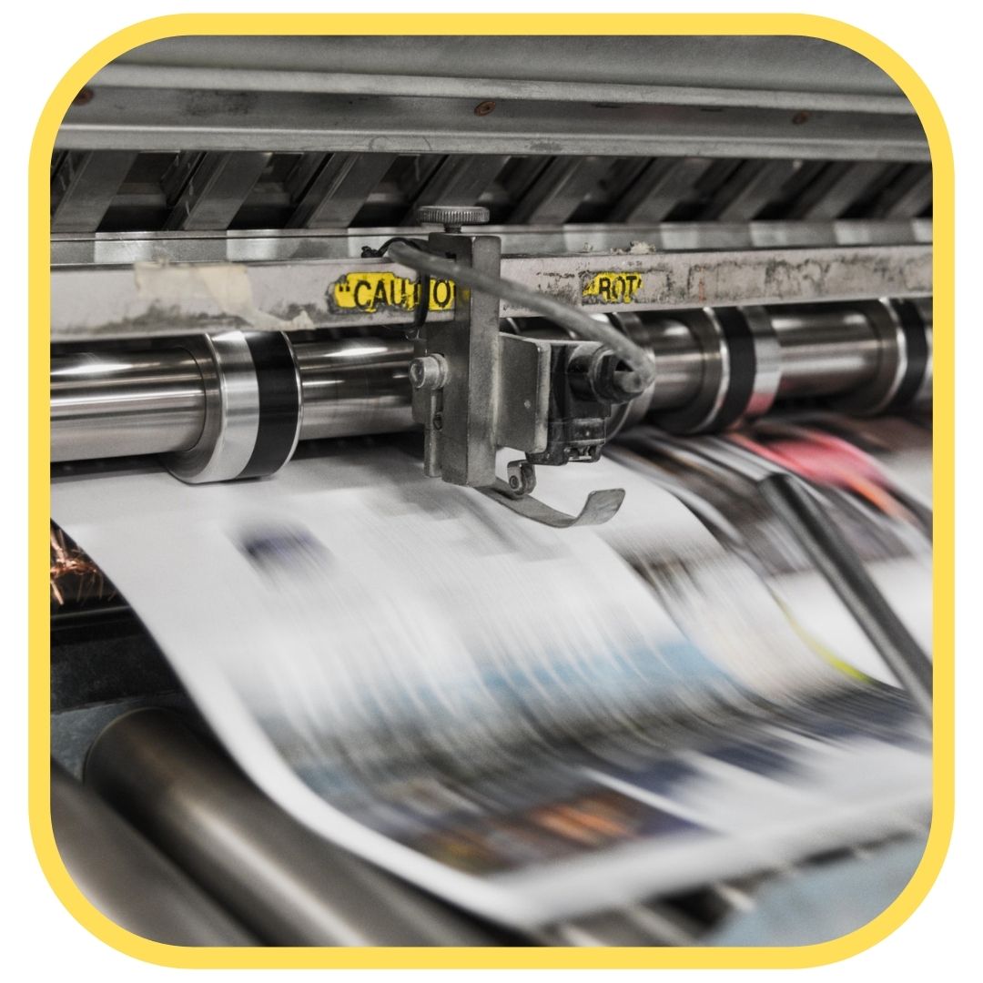A commercial printing press prints colorful, blurred pages, with CAUTION signs visible on the machine—perfect for those seeking printer ink tips. The image is bordered with a rounded yellow frame.
