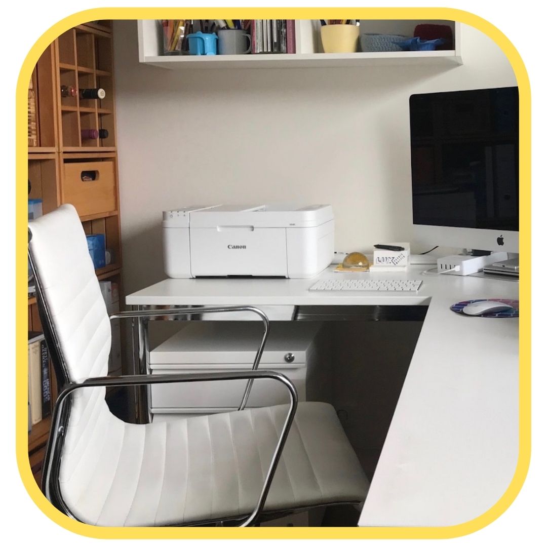 A modern home office with a white chair, a desk holding a desktop computer, keyboard, mouse, and a Canon printer. Shelves with books and containers line the wall. The neat space is perfect for using printer ink tips to save money on printer ink.